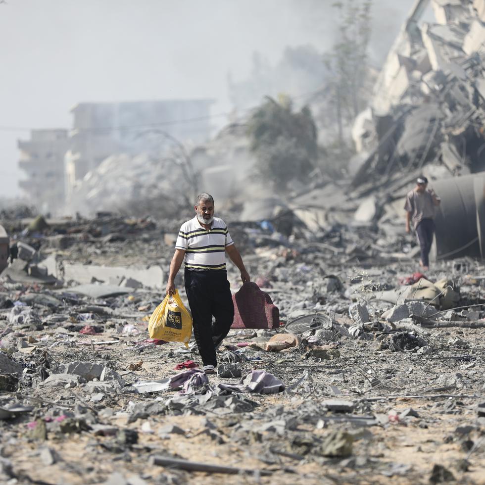 Algunos palestinos caminan junto a edificios destruidos tras un bombardeo israelí sobre Al Zahra, el viernes 20 de octubre de 2023, en las afueras de la Ciudad de Gaza.