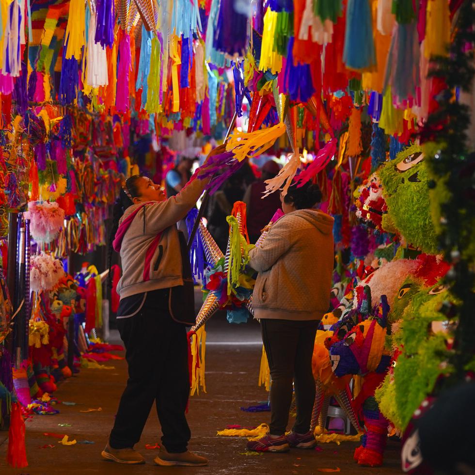 Una vendedor baja una piñata para un cliente en el mercado de Jamaica en la Ciudad de México, el jueves 14 de diciembre de 2023. La apertura de piñatas forma parte de la tradición navideña mexicana.