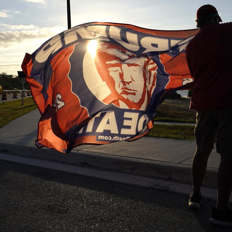 A supporter of former President Donald Trump unfurls a flag outside of Trump's Mar-a-Lago estate, Monday, March 20, 2023, in Palm Beach, Fla. (AP Photo/Lynne Sladky)