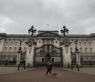Una mujer camina con un perro y un bebé frente al Palacio de Buckingham.