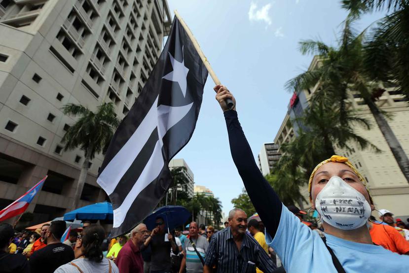 Una mujer levanta una bandera de Puerto Rico con los colores blanco y negro durante una protesta contra la Junta de Supervisión Fiscal. (GFR Media)