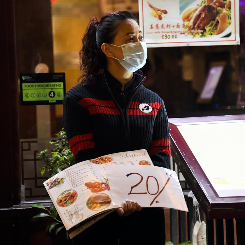 A waitress wears a protective mask as she stands at the door of a restaurant in Soho, in London, Tuesday, Sept. 22, 2020. Britain's Prime Minister, Boris Johnson, has announced that pubs and restaurants closing at 10pm, due to the spike of cases of coronavirus across the United Kingdom. (AP Photo/Alberto Pezzali)