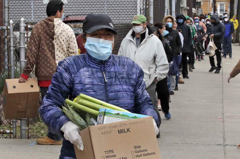 Una mujer se lleva una caja con comida mientras cientos de personas hacen fila en un centro de asistencia a los necesitados en Chelsea, Massachusetts. (AP)