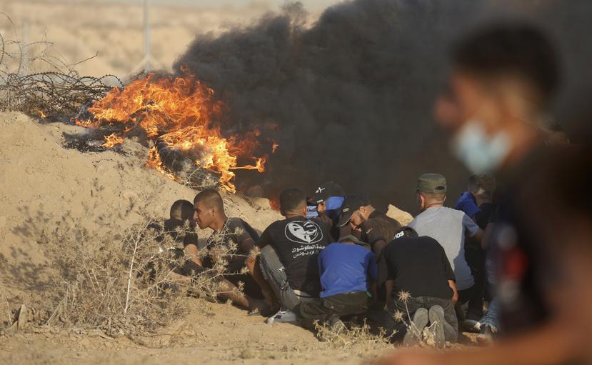 Manifestantes se protegen cerca de neumáticos en llamas en las inmediaciones de la cerca fronteriza entre Gaza e Israel durante una protesta, al este de Khan Younis, en el sur de la Franja de Gaza, el 25 de agosto de 2021.