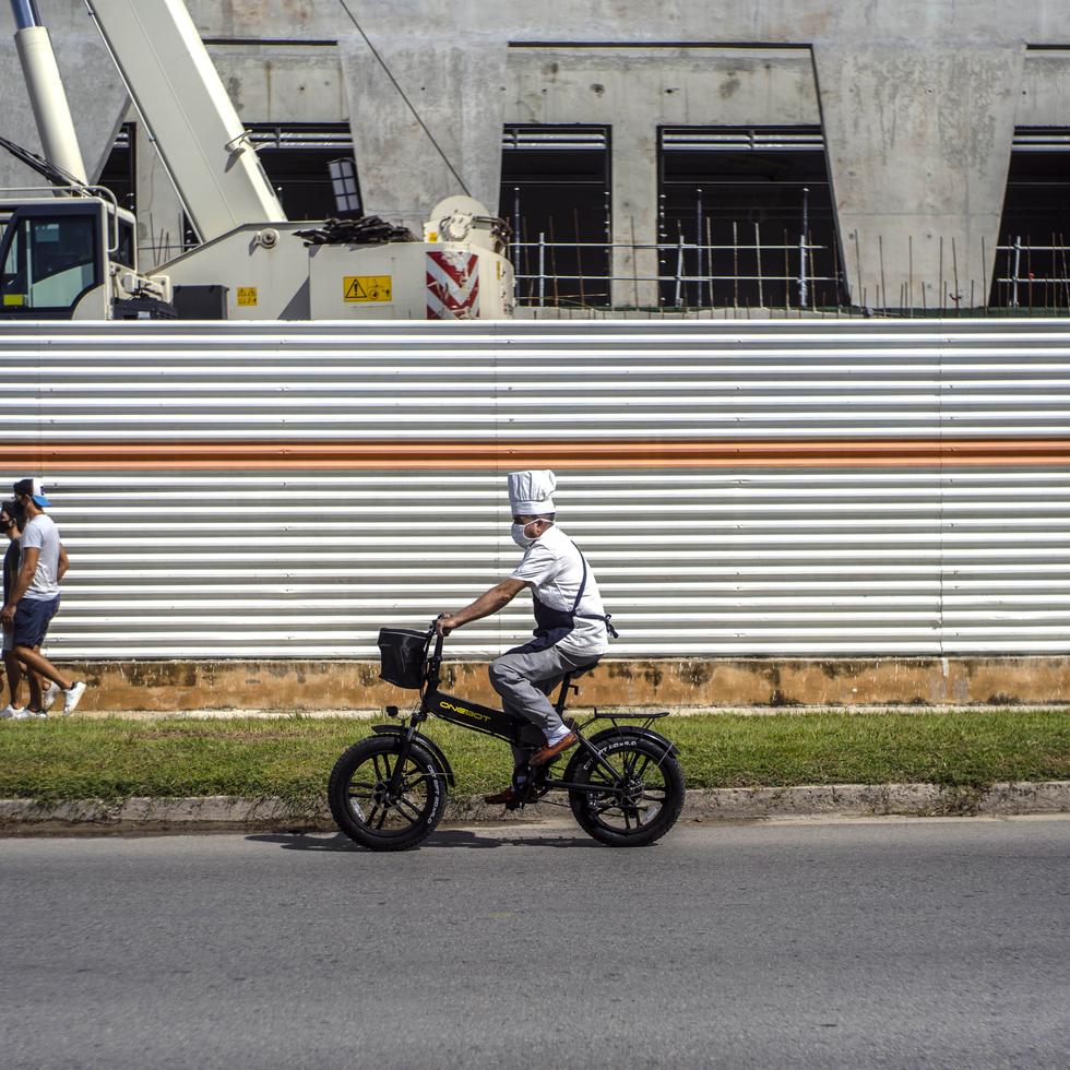 Usando una mascarilla para protegerse del nuevo coronavirus, un chef viaja a bordo de su bicicleta frente a un hotel en construcción en La Habana, Cuba, el lunes 20 de julio de 2020.
