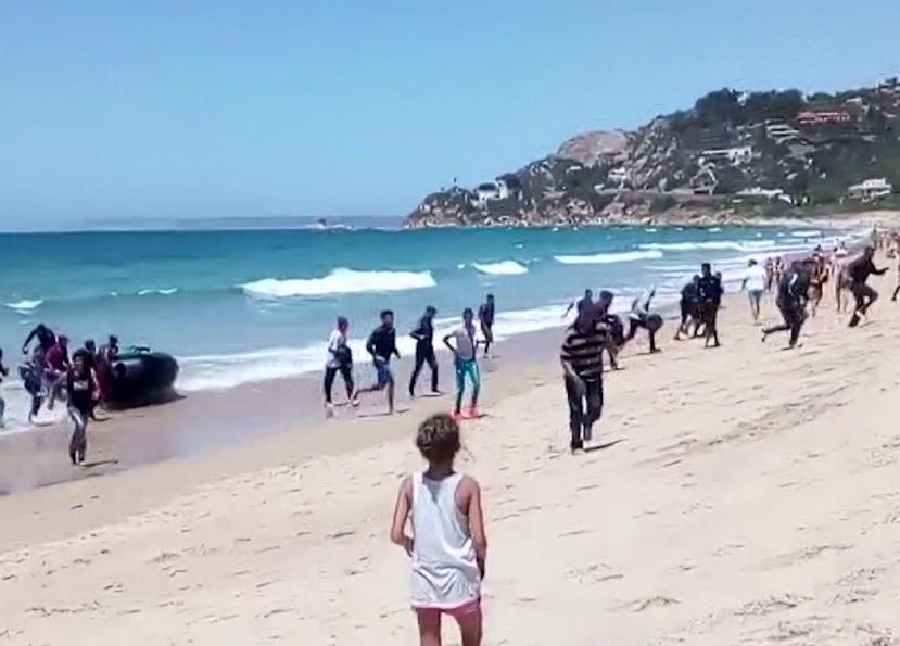 Esta foto de archivo del 9 de agosto del 2017, tomada de un video, muestra a una mujer viendo a migrantes dispersándose en la arena tras llegar a la playa en un bote de hule, en la costa de Cádiz, en el sur de España. (AP)