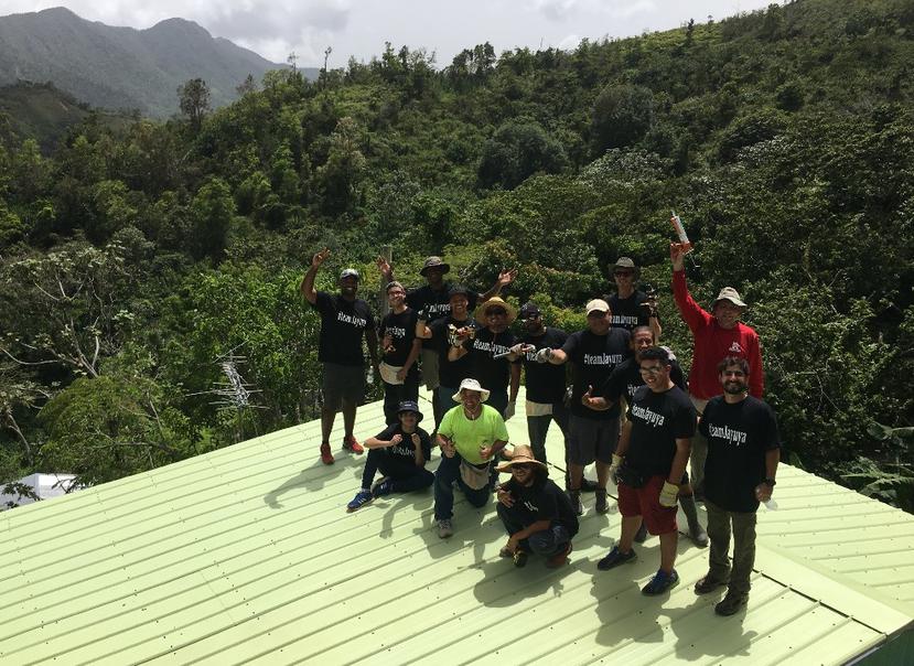 Un grupo de personas reunido sobre el techo reparado de una vivienda, en Jayuya, celebra el resultado de la obra, la que permitió eliminar un toldo azul colocado tras el azote del huracán María, en el 2017.