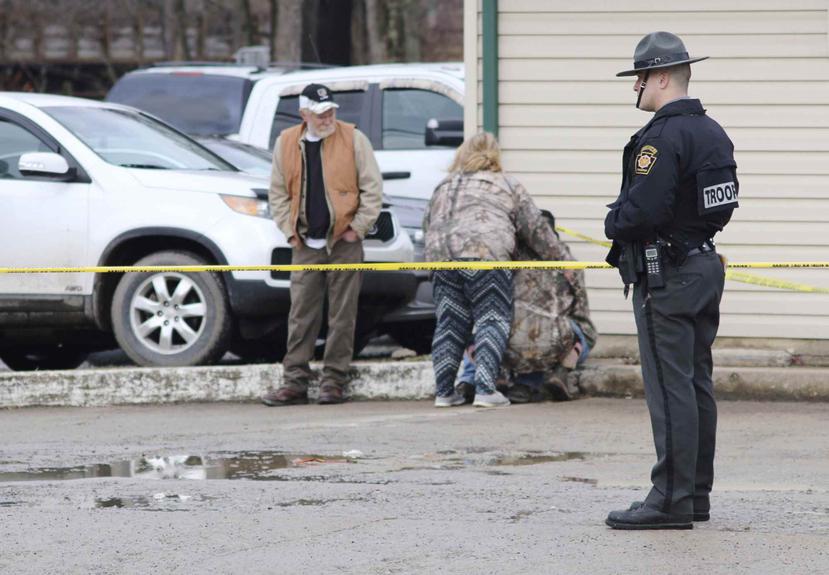Un policía monta guardia mientras otras personas se consuelan cerca del lugar de un tiroteo en un lavado de autos de Mecrof, Pensilvania. (Michael Palm / Herald-Standard vía AP)