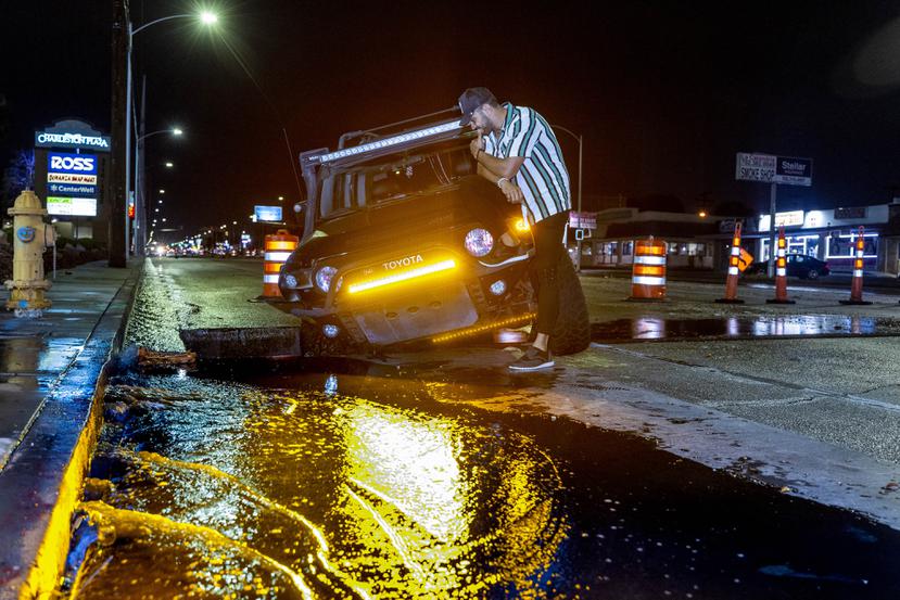 El conductor Miguel Reyes se sienta sobre su vehículo, el cual cayó en un hoyo en medio de una inundación en el Charleston Boulevard.