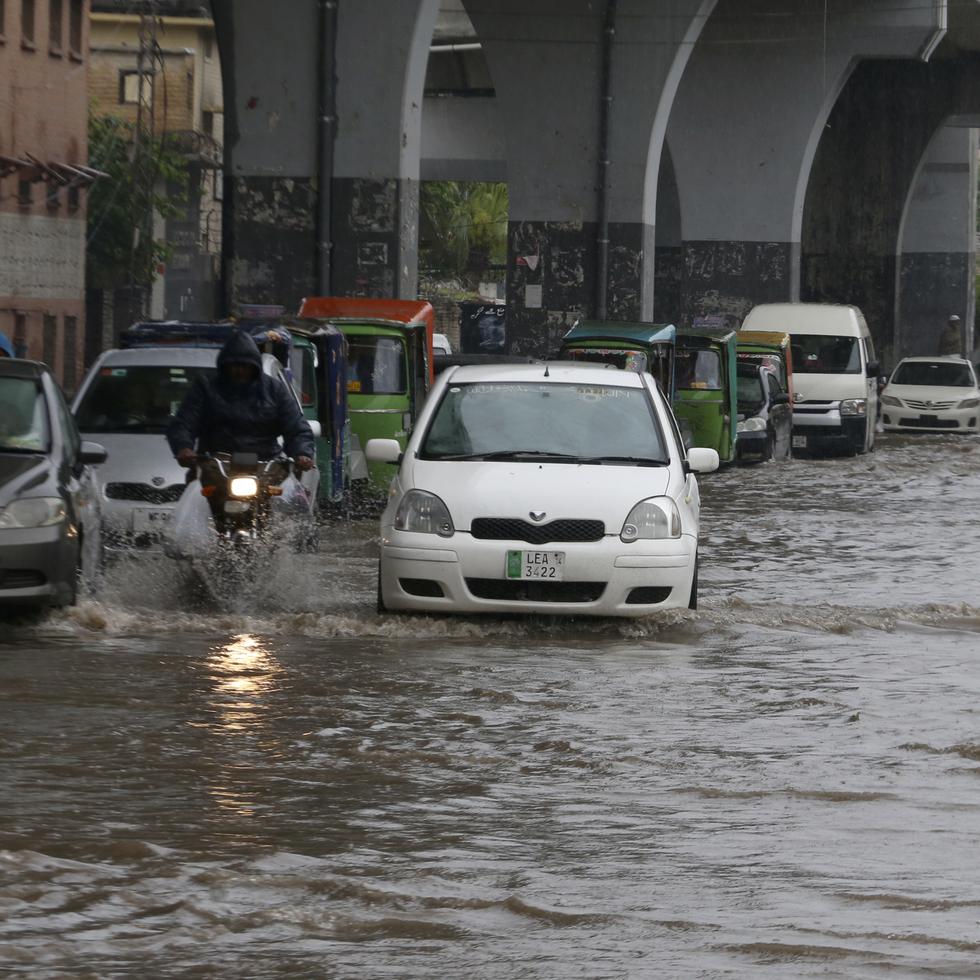 Un conductor en moto y un auto circulan por una calle inundada por las fuertes lluvias en Peshawar, Pakistán.