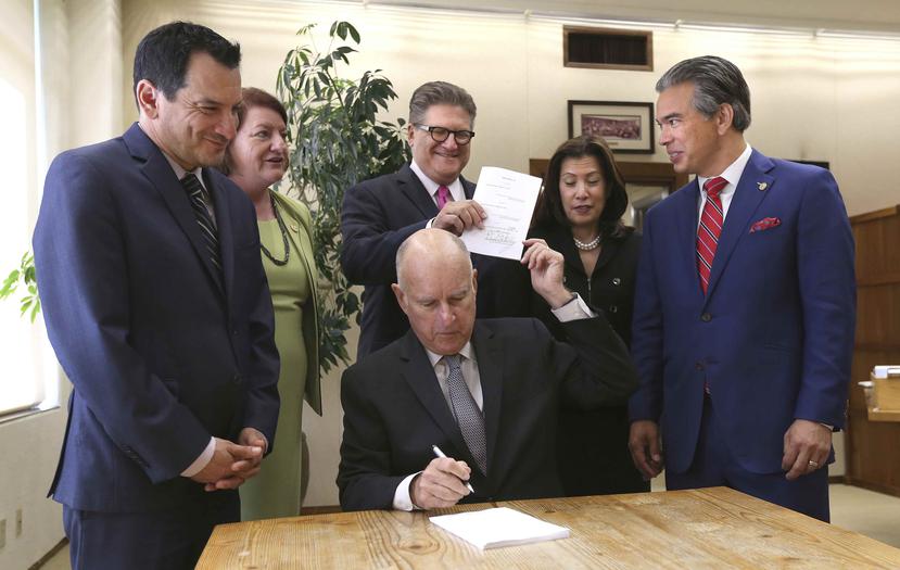 El gobernador Jerry Brown firma y entrega copia de la nueva legislación que elimina las fianzas por dinero a varios legisladores de California. (AP)