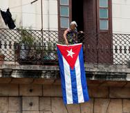 Una mujer sale al balcón donde se expone una bandera cubana, hoy en La Habana, Cuba. EFE/Ernesto Mastrascusa

