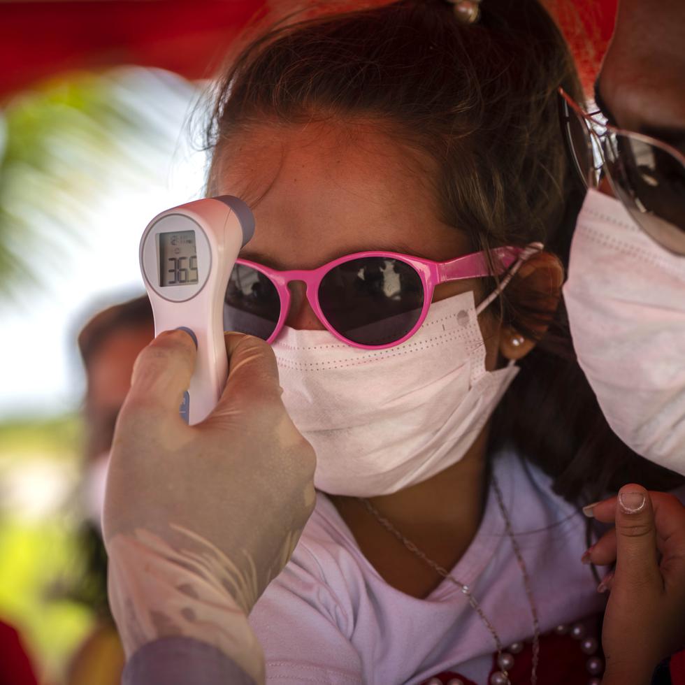 A una niña con mascarilla para protegerse del nuevo coronavirus le toman la temperatura en un puesto de control policial en la entrada de la provincia de La Habana, Cuba, el lunes 10 de agosto de 2020. (AP Foto/Ramón Espinosa)