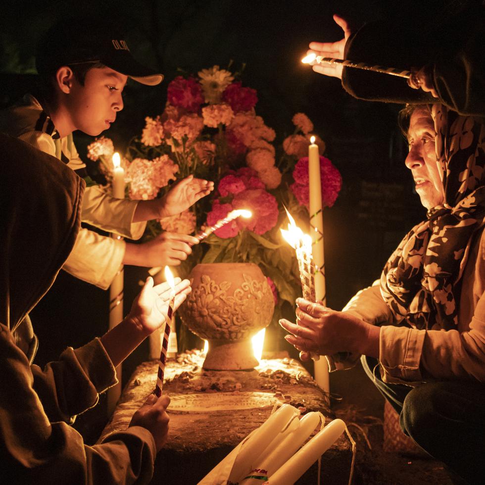 La gente sostiene velas sobre una tumba decorada con flores en un cementerio en Atzompa, México, el martes 31 de octubre de 2023 por la noche. (AP Foto/María Alferez)