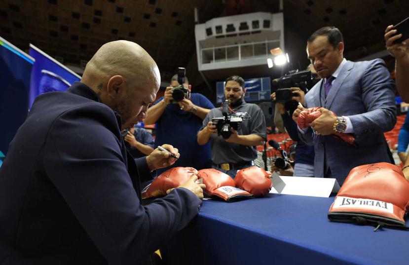 Miguel Cotto (sentado) y Juan Manuel Márquez firman unos guantes de boxeo.