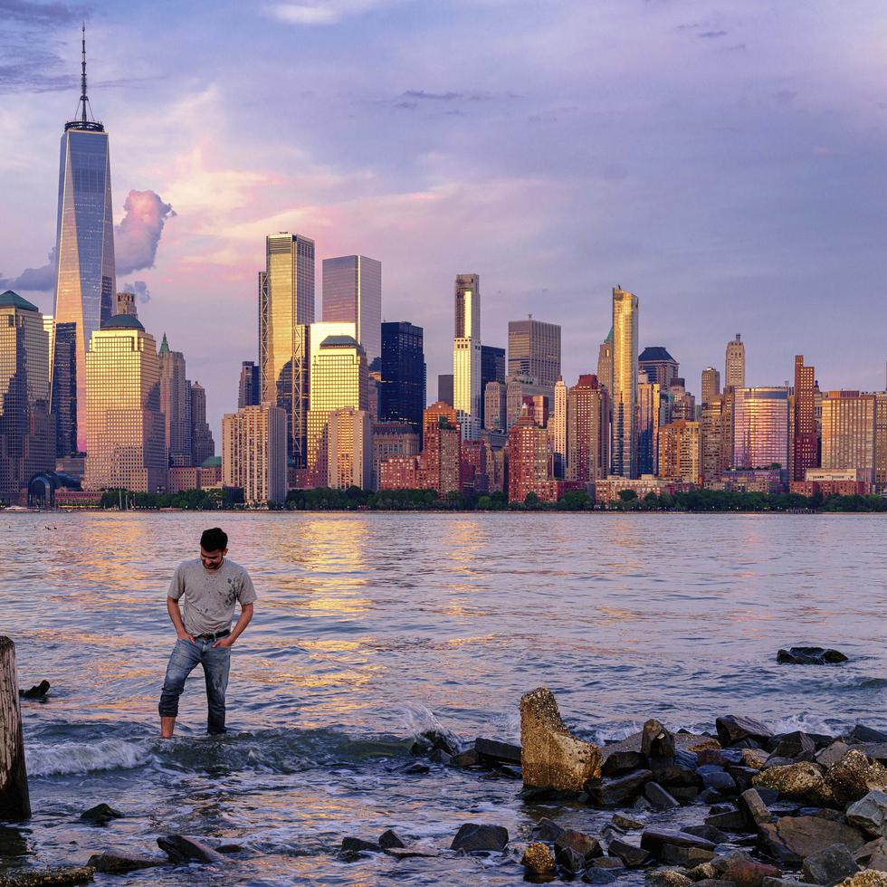 Un hombre comprueba dónde pisa mientras camina por el agua en el Canal Morris en Jersey, Nueva Jersey, mientras se pone el sol con Manhattan de fondo, el 31 de mayo de 2022. (AP Foto/J. David Ake, Archivo)
