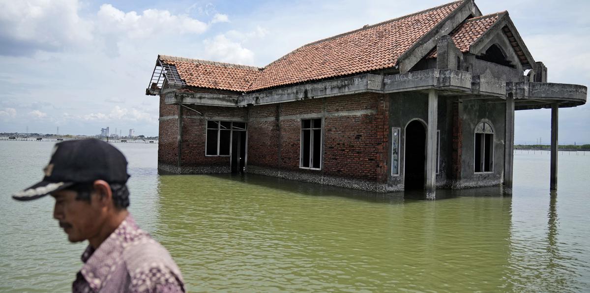 Un hombre camina frente a una casa que fue abandonada después de inundarse debido a un aumento en el nivel del mar, el 8 de noviembre de 2021, en Sidogemah, en la provincia de Java Central, Indonesia.