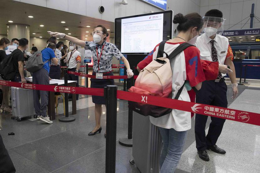 Empleados de aerolíneas redirigen a una viajera en un punto de control de pasajeros llegados de zonas de alto riesgo, para que presenten los resultados de sus pruebas de COVID-19 antes de embarcar en su vuelo desde el Aeropuerto Pekín Capital. (AP)