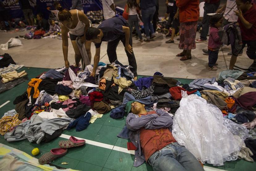 Un hombre duerme mientras otros migrantes centroamericanos recogen ropa donada en un albergue temporal, en México. (AP)