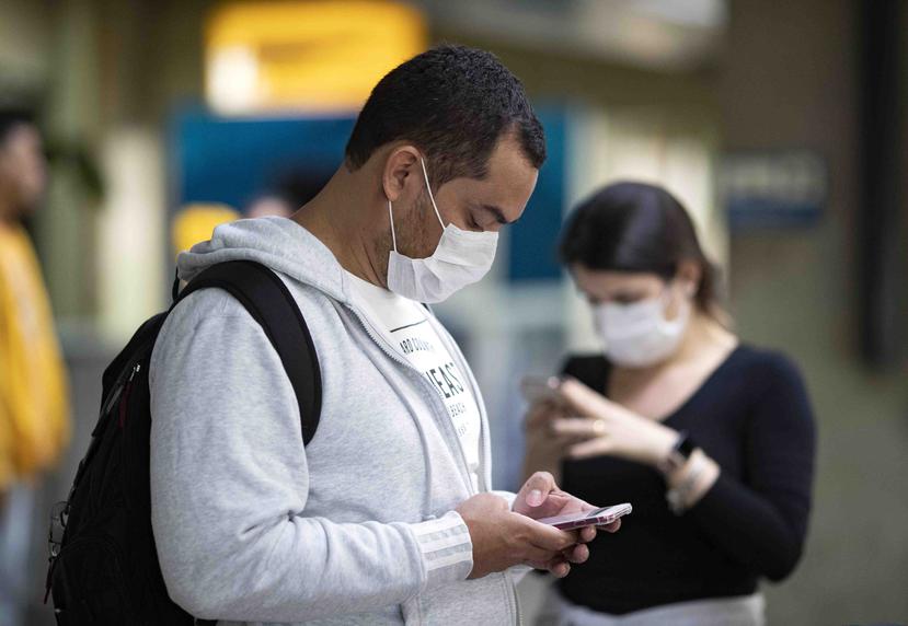 Pasajeros usando mascarillas como precaución contra el contagio del nuevo coronavirus usan sus teléfonos en el Aeropuerto Internacional de Sao Paulo, Brasil, primer país de América Latina donde se reportó un caso.