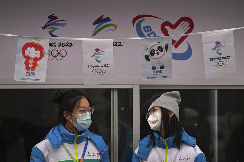 Voluntarias con mascarilla para evitar contagios de coronavirus charlan en un puesto de información para los Juegos Olímpicos de Invierno en la calle de Qianmen, un popular destino turístico en Pekín.