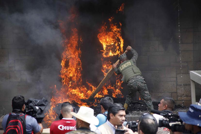 Un soldado intenta apagar el fuego frente a la embajada estadounidense en Honduras. (AP)