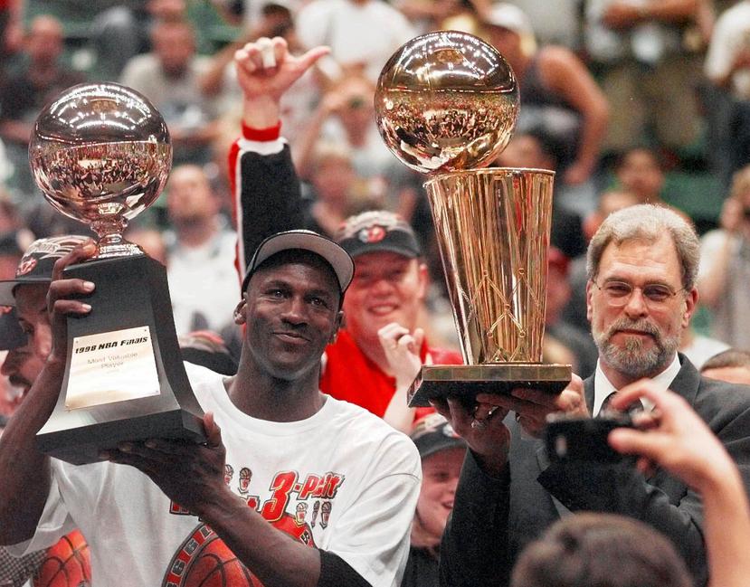 Michael Jordan alza su sexto premio de Jugador Más Valioso de la final de 1998 junto al dirigente Phil Jackson, quien carga con el trofeo de campeonato de la NBA. (AP)