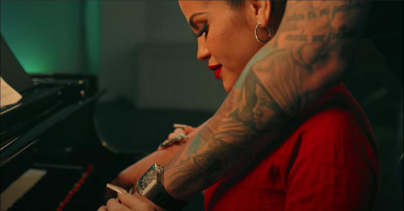 Escena en la que se observan los brazos tatuados del productor que la abraza mientras ella está frente a un piano. Aunque el rostro de Pina no se observa, sus tatuajes lo delatan.