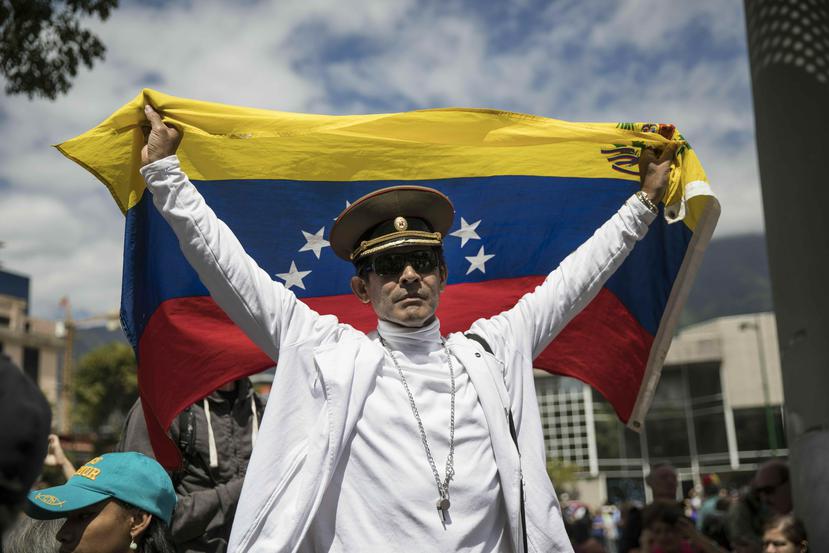 José Ramón Salas posa con una bandera de Venezuela y una gorra militar rusa en un mítin de la oposición para proponer leyes de amnistía para policías y soldados. (AP /Rodrigo Abd)