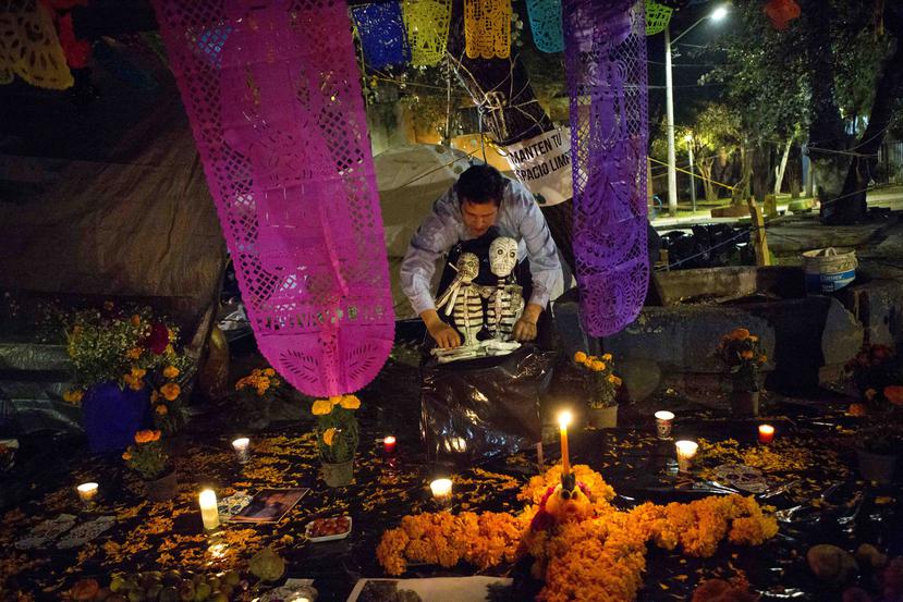 Un joven coloca dos esqueletos en un altar del Día de Muertos en medio de un campamento en Multifamiliar Tlalpan, donde nueve personas fallecieron por el colapso de un edificio en el terremoto del 19 de septiembre.