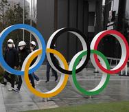 Un grupo de personas con mascarillas pasa detrás de los anillos olímpicos en Tokio. (AP)