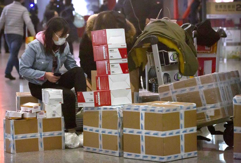 Una viajera sentada junto a cajas de mascarillas para la cara y respiradores, espera en el aeropuerto internacional de Beijing, en China.