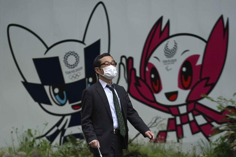 Un hombre con una mascarilla camina por las calles de Tokio frente a un mural con las mascotas Miraitowa y Someity.