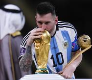 Lionel Messi besa el trofeo de la Copa del Mundo mientras sostiene el premio al mejor jugador del torneo.