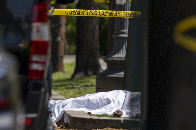Una víctima bajo una sábana mientras agentes del Departamento de Policía Metropolitana investigan la escena de un tiroteo frente a la funeraria Stewart.