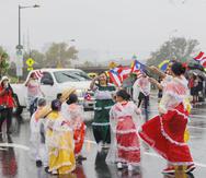 Varias niñas y niños vestidos con trajes típicos bailan bajo la lluvia durante la parada celebrada esta tarde.