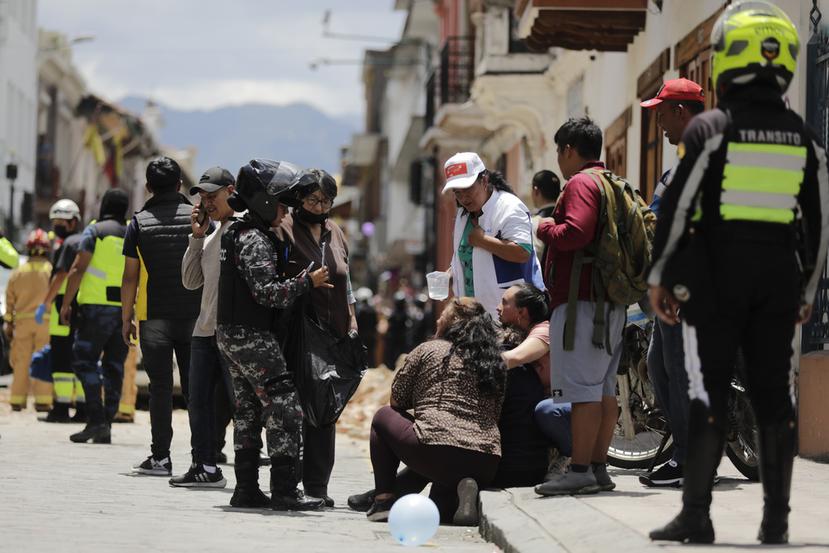 La policía habla con las personas junto al sitio donde un automóvil fue aplastado por los escombros después de un fuerte sismo que sacudió Cuenca, Ecuador, el sábado 18 de marzo de 2023. (Foto AP/Xavier Caivinagua)