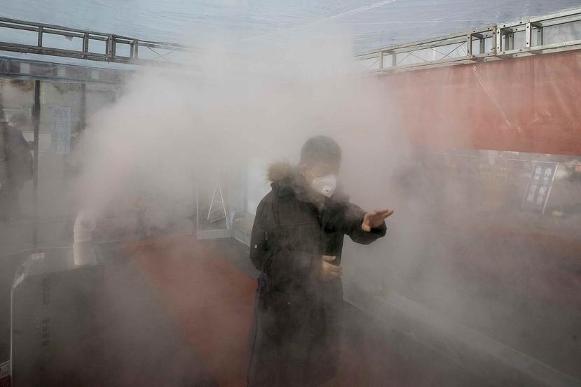 Un hombre atraviesa una nube de desinfectante pulverizado para regresar a casa en un complejo residencial en la ciudad de Tianjin, en el norte de China. (AP)