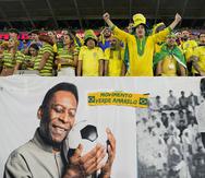 Aficionados de Brasil alientan a la selección detrás de un cartel con imágenes de Pelé, el lunes 5 de diciembre de 2022, antes de un partido del Mundial ante Corea del Sur en Al Rayán, Qatar (AP Foto/Martin Meissner)