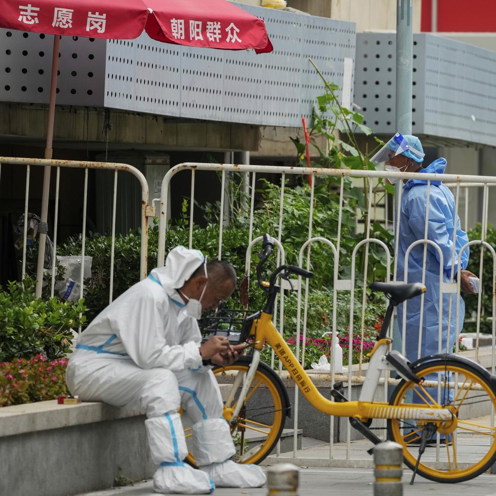 Trabajadores observan un vecindario que fue aislado como parte de las restricciones implementadas por un nuevo brote de COVID-19 en Pekín.