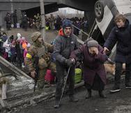 Una anciana recibe ayuda mientras cruza el río Irvin, bajo un puente destruido por un ataque aéreo ruso, mientras civiles huyen de la localidad de Irpin, Ucrania, el 5 de marzo de 2022.