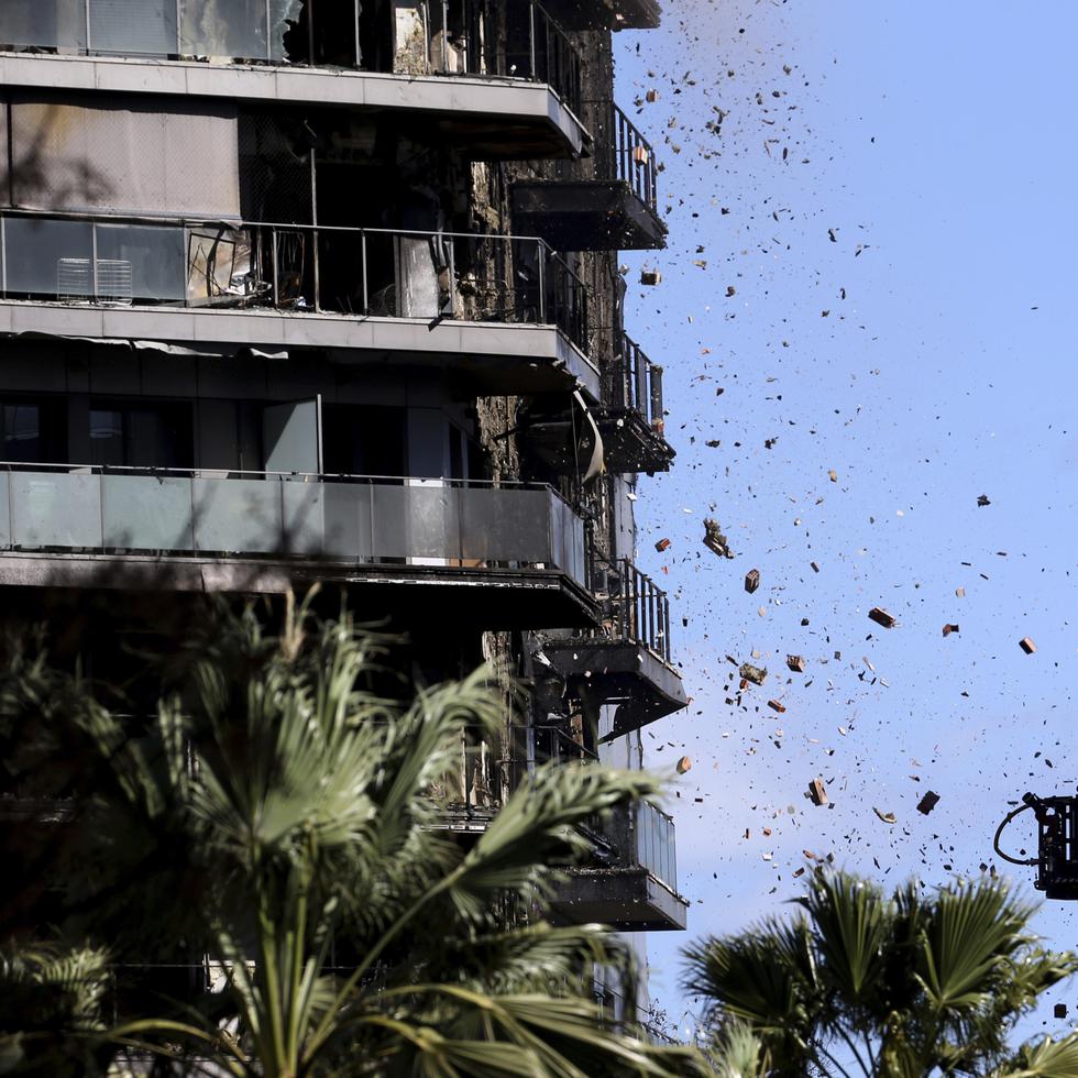 Escombros caen frente a los bomberos que realizan tareas en un edificio de apartamentos incendiado, en Valencia, España.