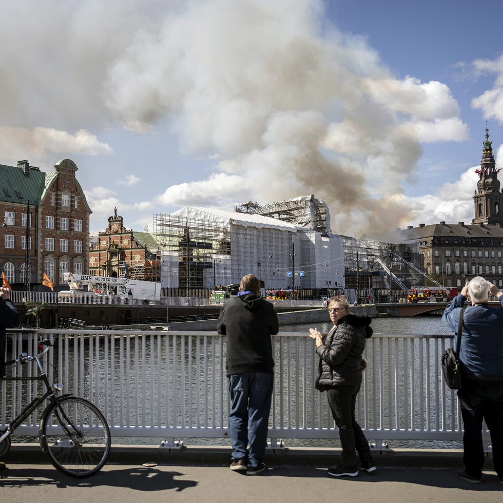 La gente toma fotografías mientras los bomberos apagan un incendio en el antiguo edificio de la Bolsa de Valores de Copenhague, Dinamarca.