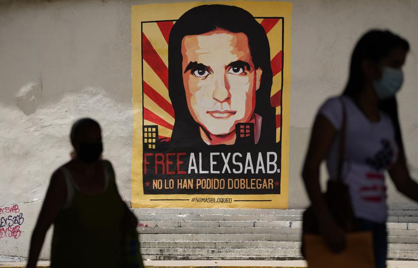 Personas camina cerca de un cartel que pide la liberación del empresario colombiano y enviado especial del gobierno venezolano, Alex Saab, en Caracas, Venezuela.