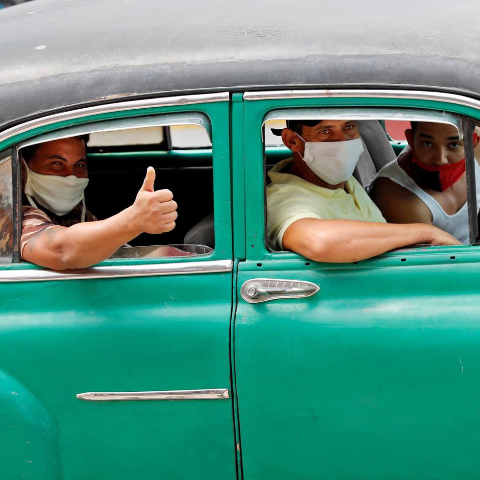 Varias personas con mascarillas pasean en un auto clásico por una calle de La Habana.