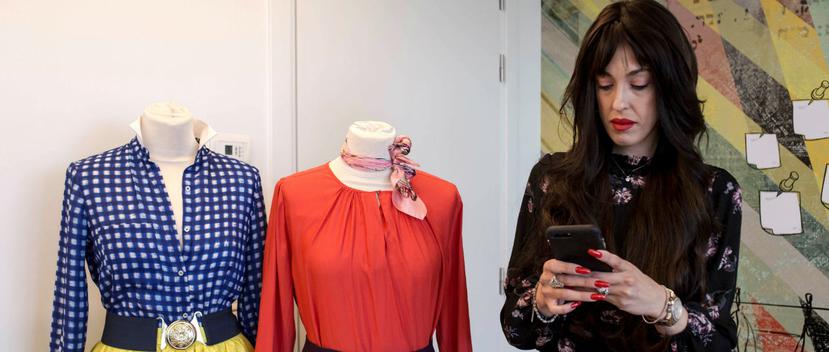 La estilista y profesora de moda haredi, Miri Beilin, ojea su móvil junto a dos diseños pensados para las mujeres ultraortodoxas. (Foto: EFE/Patricia Martínez)