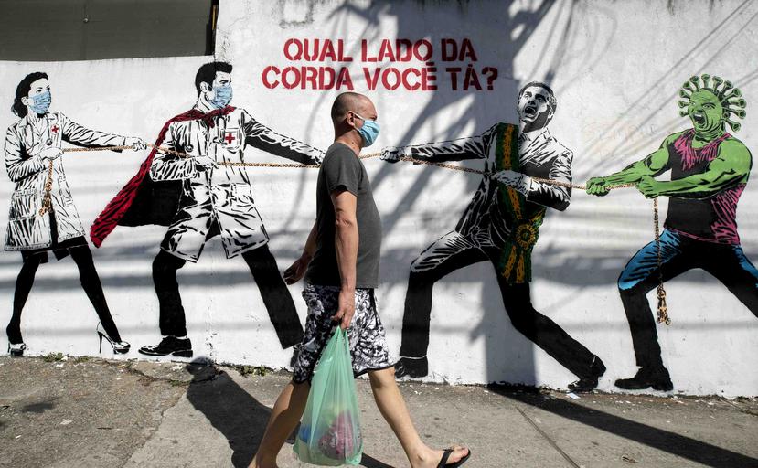 Un hombre que porta una mascarilla camina el viernes 19 de junio de 2020 frente a un mural en Sao Paulo, Brasil, que describe una lucha entre trabajadores de salud por un lado y el presidente Jair Bolsonaro y un personaje que representa al coronavirus por