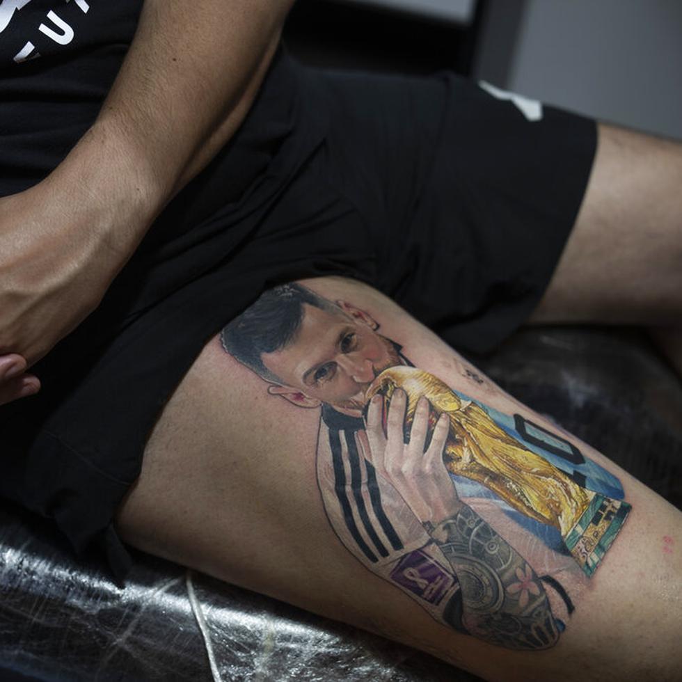 Sebastián Fernández descansa mientras el artista César "Yeyo" Molina le tatúa en la pierna una imagen del futbolista Lionel Messi besando la Copa del Mundo en Buenos Aires, Argentina, el jueves 29 de diciembre de 2022.