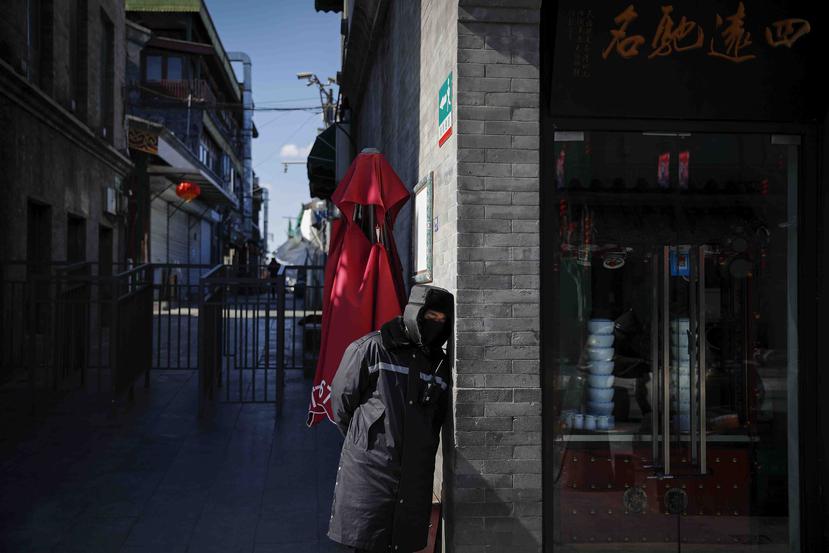 Un guardia de seguridad con el rostro cubierto para protegerse del coronavirus descansa junto a una tienda cerrada en la calle Qianmen, un popular destino turístico de Pekín. (AP / Andy Wong)