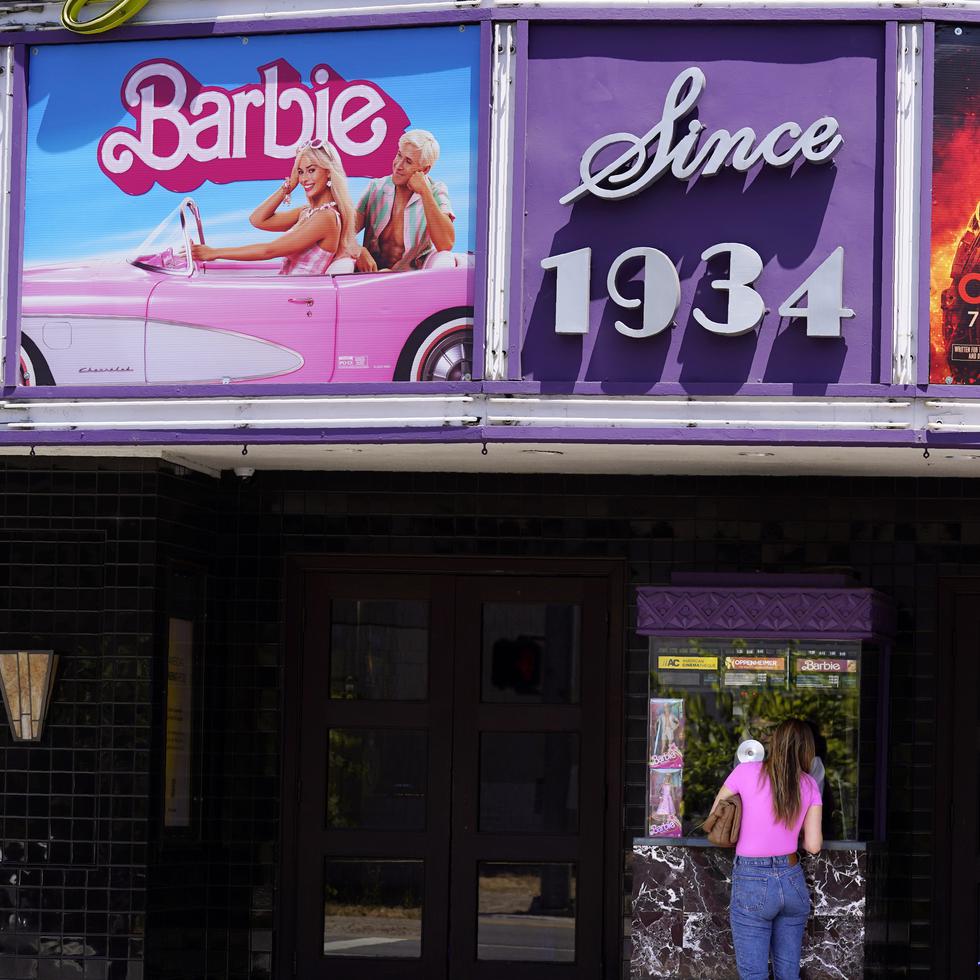 Una persona compra boletos de cine debajo de un cartel con las películas "Barbie" y "Oppenheimer" en el cine Los Feliz, en Los Ángeles.